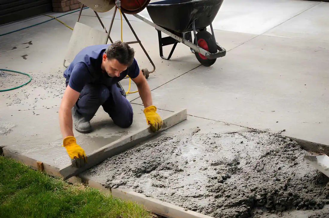 Worker smoothing fresh concrete for a residential driveway installation.
