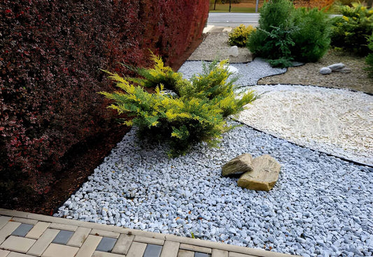 Landscaped garden with decorative rocks for mulch, small shrubs, and stone edging beside a textured wall.